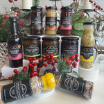 Assorted jars and bottles of sauces and vinegars on a decorative surface with red berries and greenery.