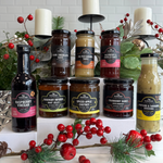 The Summer Essentials gift hamper for those who deserve the finest in gifts and the finest in flavours. Packed full of Australian made gourmet goodness, there's artisan goodness for everyone and every occasion, all presented in a Black premium gift box.
Assorted jars and bottles of sauces and vinegars on a decorative stand with Christmas decorations.