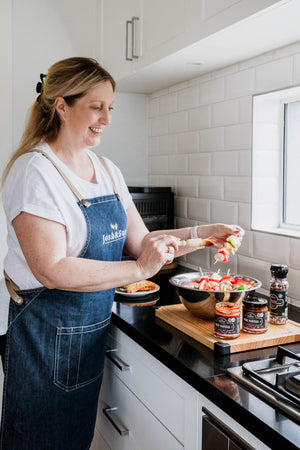
                  
                    Woman in a kitchen preparing food, wearing a blue apron.
                  
                